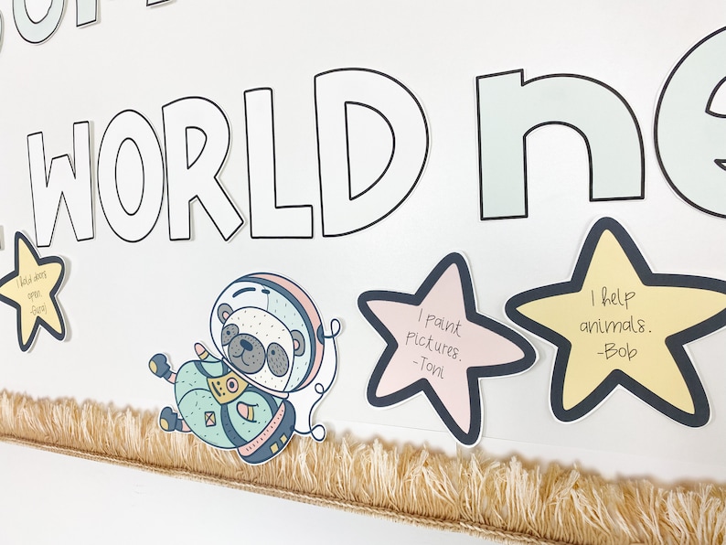 Puede incluir: Un tablero de anuncios blanco con las palabras "Our World" en letras negras delineadas. Hay tres recortes en forma de estrella amarilla con mensajes escritos a mano. Uno dice "Ayudo a los animales - Bob", otro dice "Pinto cuadros - Toni", y el &uacute;ltimo dice "Abro puertas - Carl". Hay una ilustraci&oacute;n de dibujos animados de un oso con un traje espacial.