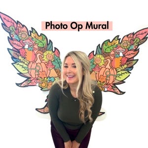 Puede incluir: Una mujer se encuentra frente a un mural colorido con temática otoñal con el texto "Photo Op Mural". El mural presenta hojas, calabazas, girasoles y otros elementos otoñales.