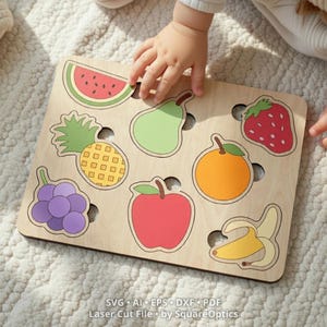 Peut inclure: Un plateau de puzzle en bois avec des illustrations de fruits colorés, notamment une tranche de pastèque, une poire, une fraise, un ananas, une orange, du raisin, une pomme et une banane. Le texte en bas indique SVG AI EPS DXF PDF Laser Cut File by SquareOptics.