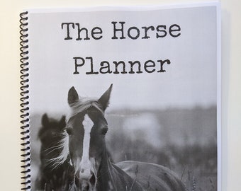 May include: A spiral-bound planner titled "The Horse Planner" with a black and white image of a horse in a field. The horse has a white blaze and is surrounded by tall grass. The cover is white with black text.
