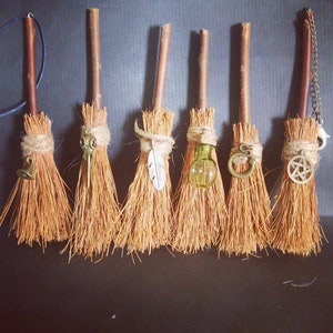May include: Seven miniature broomsticks with different decorative charms, including a bell, a bird mask, a feather, a potion bottle, a snake, a pentagram, and a crescent moon.