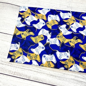 May include: Blue fabric with a repeating pattern of white and gold video game controllers.