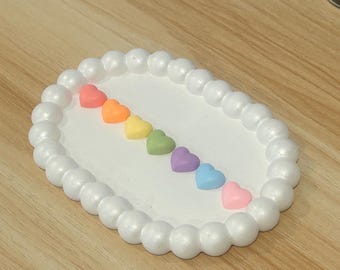 Puede incluir: Un plato blanco ovalado con un borde de cuentas, decorado con un arcoíris de caramelos en forma de corazón.