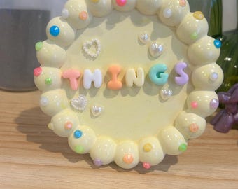 Puede incluir: Un letrero circular amarillo con un borde blanco y puntos de colores. El letrero dice "THINGS" en letras de colores.