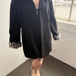May include: A black long-sleeved coat with a leopard print faux fur collar and cuffs. The coat has a button closure and a fitted silhouette.