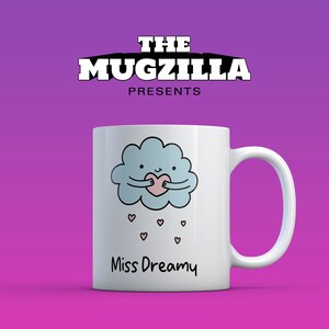 May include: White ceramic mug with a cartoon cloud holding a pink heart, with small hearts falling below. The mug has the text "Miss Dreamy" and the logo "THE MUGZILLA PRESENTS".