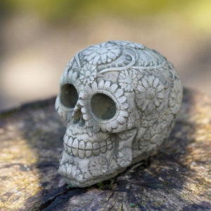 Può includere: Un teschio di zucchero decorativo grigio con dettagli floreali. Il teschio è fatto di un materiale strutturato e ha un design dettagliato.