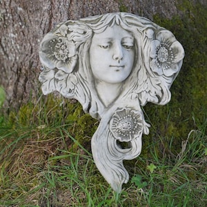 Peut inclure: Une sculpture en pierre blanche représentant le visage d'une femme avec des fleurs dans les cheveux. La sculpture est détaillée et a un aspect réaliste.