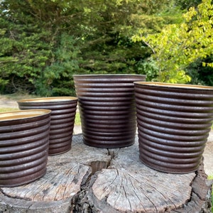 Op de afbeelding: Vier bruine metalen potten met een gouden rand. De potten zijn gerangschikt van groot naar klein op een boomstronk.