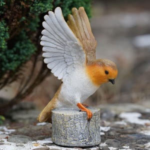 May include: A detailed figurine of a robin with outstretched wings, perched on a faux wooden stump. The bird features a vibrant orange breast, brown and white wings, and a black beak. The sculpture is designed for garden or home decor.