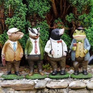 Könnte beinhalten: Vier anthropomorphe Tierfiguren in einer Reihe. Von links nach rechts: eine Maus in beigem Karoblazer und Mütze, ein Dachs in grüner Jacke und roter Krawatte, ein Maulwurf im weißen Hemd mit Hosenträgern und ein Frosch in blauer Jacke und Zylinder.