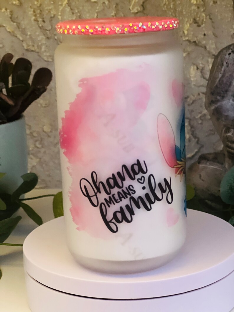 May include: White ceramic jar with a pink and blue watercolor design. The jar has a pink glitter lid and features the text "Ohana means family" in black lettering.