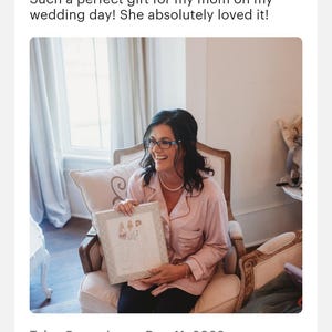 K&ouml;nnte beinhalten: Ein Aquarellbild von drei Personen in Hochzeitskleidung, gerahmt in einem wei&szlig;en Rahmen mit einem dekorativen Rand. Das Bild wird von einer Person in einem rosa Morgenmantel gehalten, die auf einem Stuhl sitzt.