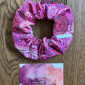 May include: Pink and white patterned hair scrunchie with the text "Malu Dreamer" on the side. The scrunchie is handmade and features an Aboriginal-inspired design.