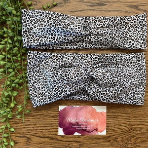 May include: Two leopard print headbands with a knotted design. The headbands feature a white background with black and brown spots. A business card with the text "Malu Dreamer" is also visible.