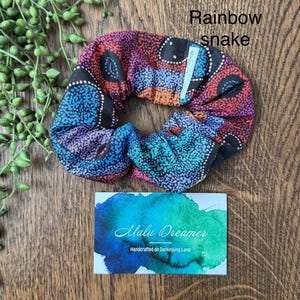 May include: A fabric hair scrunchie featuring a multicolored dot pattern in shades of red, orange, blue, and purple, labeled Rainbow snake. A rectangular card displays the text Malu Dreamer Handcrafted on Darkinjung Land.