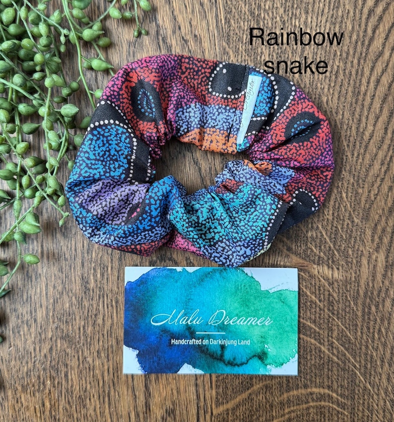May include: A fabric hair scrunchie featuring a multicolored dot pattern in shades of red, orange, blue, and purple, labeled Rainbow snake. A rectangular card displays the text Malu Dreamer Handcrafted on Darkinjung Land.