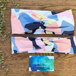 May include: Two fabric headbands featuring a twisted knot design and a multi-colored abstract pattern in shades of navy blue, light pink, pale yellow, and white. A rectangular card with a blue watercolor background and the text Malu Dreamer is included.