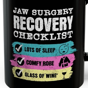 Puede incluir: Taza de café negra con texto blanco que dice "Jaw Surgery Recovery Checklist" con tres casillas de verificación e iconos. Las casillas de verificación están marcadas y el texto junto a ellas dice "Lots of Sleep", "Comfy Robe" y "Glass of Wine".