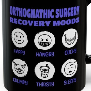 Puede incluir: Taza de café negra con un diseño blanco de diferentes expresiones faciales y el texto "Orthognathic Surgery Recovery Moods".