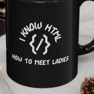 Könnte beinhalten: Schwarze Kaffeetasse mit weißem Text, der "Ich kenne HTML, wie man Frauen kennenlernt" lautet, mit einem pixeligen Code-Klammer-Symbol.