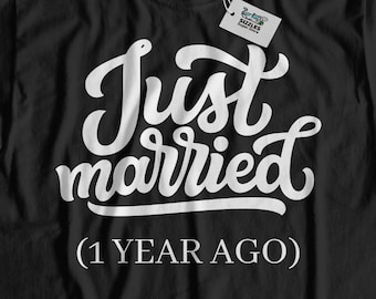May include: Black t-shirt with the white text "Just married (1 YEAR AGO)". The shirt has a tag attached. The shirt is displayed on a light wood surface.