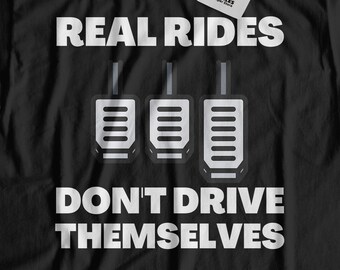 Könnte beinhalten: Schwarzes T-Shirt mit weißem Text, der "REAL RIDES DON'T DRIVE THEMSELVES" lautet. Der Text wird von einer Grafik mit drei Autopedalen begleitet.