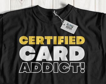 May include: Black t-shirt with the text "CERTIFIED CARD ADDICT!" in white and gold lettering.