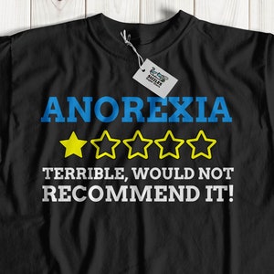 May include: Black t-shirt with a blue and white graphic that says "ANOREXIA" with five yellow stars and the text "TERRIBLE, WOULD NOT RECOMMEND IT!"