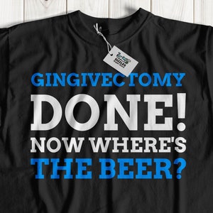 May include: Black t-shirt with the text "GINGIVECTOMY DONE! NOW WHERE'S THE BEER?" in white and blue lettering. The shirt has a tag attached. The shirt is displayed on a light wood surface.