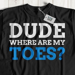May include: Black t-shirt with the text "DUDE WHERE ARE MY TOES?" in white and blue block letters. The shirt is displayed on a light wood grain surface.