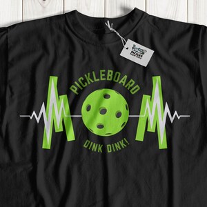 May include: Black t-shirt with a green pickleball graphic and the text "Pickleboard Dink Dink!"