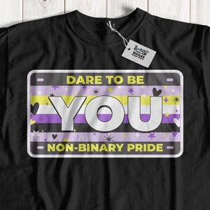 May include: Black t-shirt with a graphic of a license plate that says "Dare to be You - Non-Binary Pride". The license plate has a yellow, white, and purple stripe, hearts, and stars.