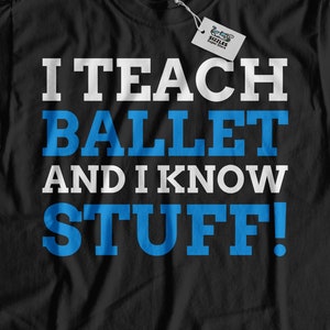 May include: Black t-shirt with the text "I TEACH BALLET AND I KNOW STUFF!" in white and blue block letters. The shirt has a crew neck and a tag attached. The shirt is displayed on a light wood surface.
