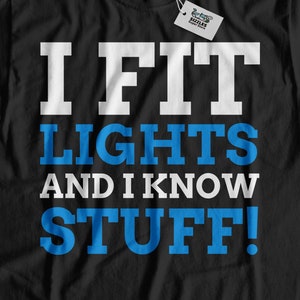 May include: Black t-shirt with white text that reads "I FIT LIGHTS AND I KNOW STUFF!" The text is in a bold, blocky font. The words "LIGHTS" and "STUFF" are in blue.