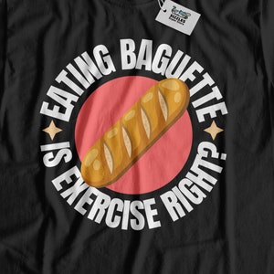 Op de afbeelding: Zwart T-shirt met een witte cirkelvormige afbeelding met de tekst "Baguette eten is sport, toch?" met een cartoon-baguette in de cirkel.