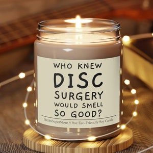 May include: A brown soy candle with a white label that reads "WHO KNEW DISC SURGERY WOULD SMELL SO GOOD?"  Sizzle SuperStore // 9oz Eco-Friendly Soy Candle