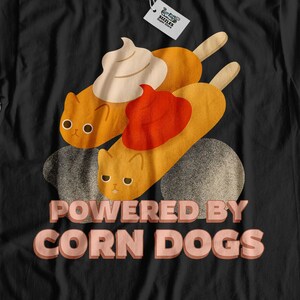 May include: Black t-shirt with a graphic of two cartoon cats eating corn dogs. The text "Powered by Corn Dogs" is printed in pink below the cats.