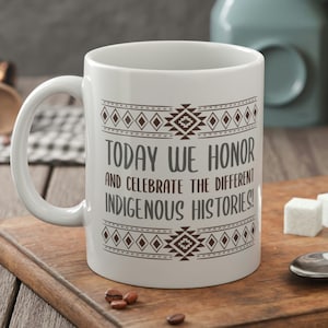 Puede incluir: Taza de cerámica blanca con un patrón geométrico marrón alrededor de la parte superior e inferior. La taza tiene un asa negra y dice "TODAY WE HONOR AND CELEBRATE THE DIFFERENT INDIGENOUS HISTORIES!"