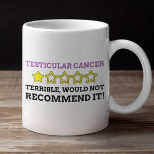 May include: White ceramic coffee mug with a black graphic that reads "Testicular Cancer" with five yellow stars and the text "Terrible, would not recommend it!"