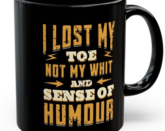 May include: Black coffee mug with a white design that says "I lost my toe not my wit and sense of humour".
