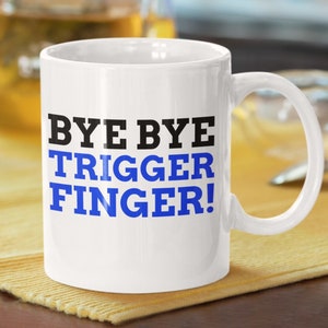 Può includere: Tazza da caffè in ceramica bianca con testo nero e blu che recita "Bye Bye Trigger Finger!"