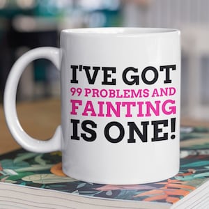 May include: White ceramic mug with a black and pink design. The mug reads "I've got 99 problems and fainting is one!"
