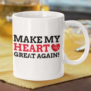 May include: White ceramic coffee mug with black text that reads "Make My Heart Great Again!" with a red heart and EKG symbol.