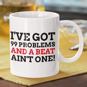 May include: White ceramic coffee mug with black text that reads "I've got 99 problems and a beat ain't one!" The text "beat" is in red.