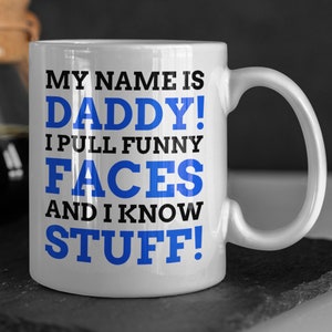 Puede incluir: Taza de café de cerámica blanca con un diseño azul y negro. El texto en la taza dice "My name is Daddy! I pull funny faces and I know stuff!"