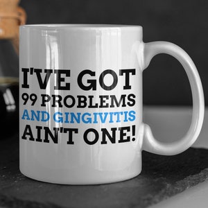 May include: White ceramic coffee mug with a black and blue design. The mug reads "I've got 99 problems and gingivitis ain't one!"