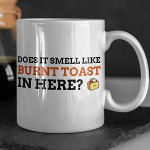 May include: White ceramic mug with black text that reads "Does it smell like burnt toast in here?" with a cartoon image of a toaster and burnt toast.