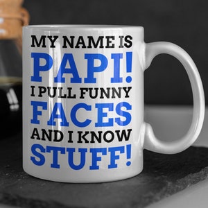 May include: White ceramic coffee mug with a blue and black design. The mug reads "My name is Papi! I pull funny faces and I know stuff!"