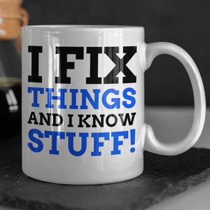 Könnte beinhalten: Weiße Keramiktasse mit einem schwarzen und blauen Design. Die Tasse sagt "Ich repariere Dinge und ich weiß, was ich tue!"